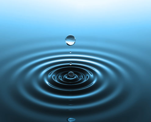 Drop of water falling into water with concentric ripples on the surface in a cool blue color