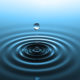 Drop of water falling into water with concentric ripples on the surface in a cool blue color